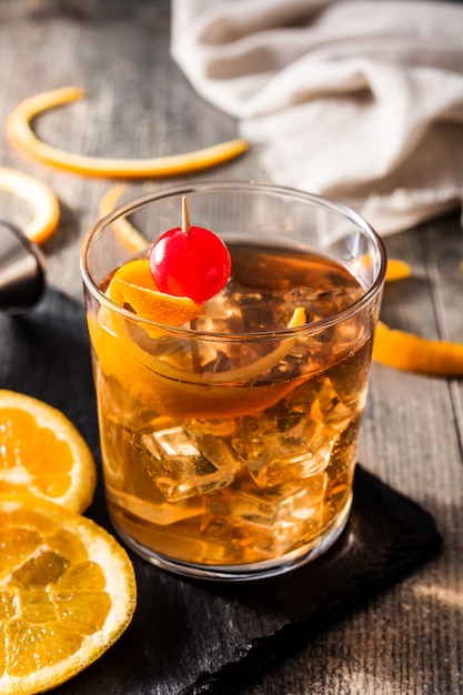Ouderwetse cocktail met sinaasappel en kers op houten lijst