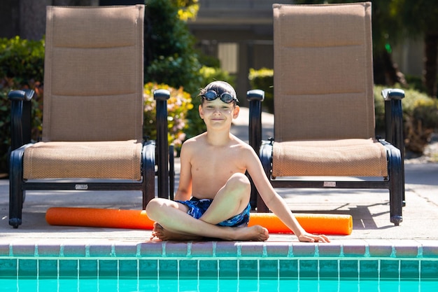屋外の夏のアクティビティ楽しい健康と休暇のコンセプト水泳メガネをかけた 8 歳の少年は、暑い夏の日にプールの近くに座っています。