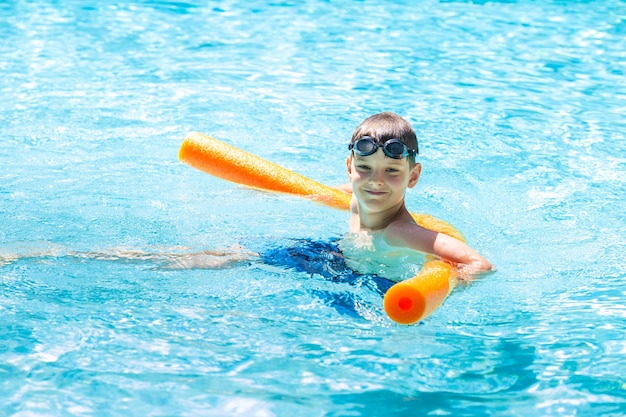 Photo oudoor summer activity concept of fun health and vacation happy smiling boy eight years old in swim glasses swim in the pool with noodle in hot summer day