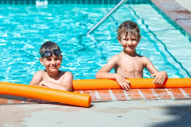 Foto oudoor zomeractiviteit concept van leuke gezondheid en vakantie een gelukkige broers van acht en vijf jaar oud in een zwembril houden zich vast aan de rand van het zwembad op een hete zomerdag