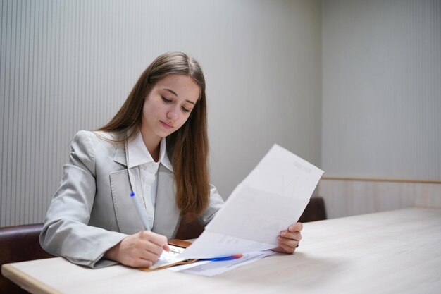 Oung concentrated businesswoman holding pen filling document or tax form making notes on paper