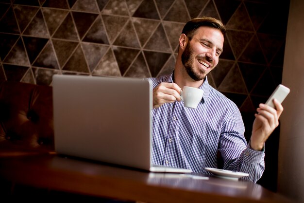 Oung man zit in cafés, koffie drinken en kijken met een glimlach op een mobiele telefoon