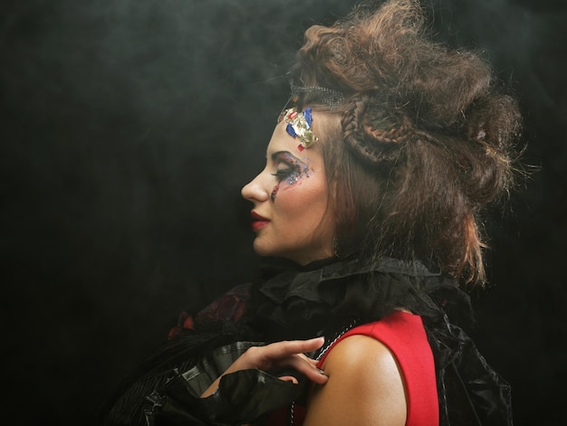 Oung modieuze vrouw met creatieve make-up en kapsel poseren op donkere achtergrond