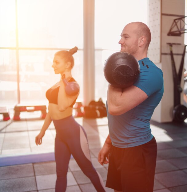 Ð¡ouple functional training. Sporty man and fit woman doing exercise with kettlebell in gym