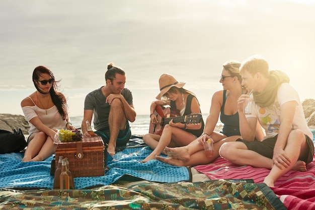 Наши лучшие воспоминания связаны с пляжем. Группа счастливых молодых друзей вместе наслаждается пикником на пляже.