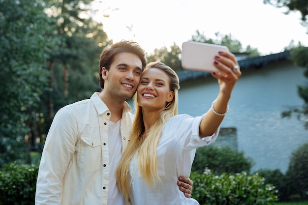 Our photo. Joyful nice couple standing together while taking selfie of them