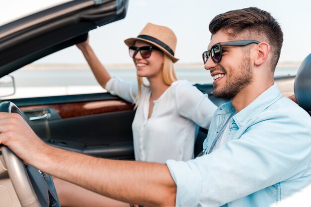 Our time for adventure. Side view of joyful young man driving convertible while his girlfriend sitting near on the front seat