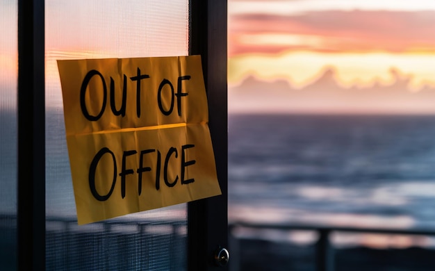 Photo out of office note paper message sign on the door with a blurred sea horizon sunset sky background