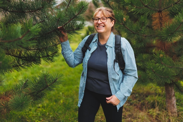 Outddor portrait of happy European female pensioner with backpack enjoying beautiful nature while nordic walking Aging people active lifestyle and health concept