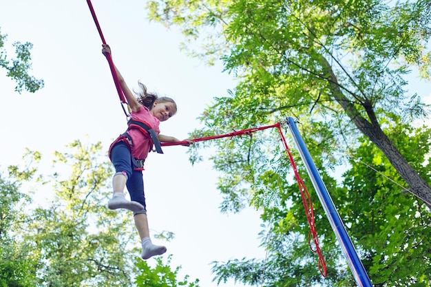 Outdoor actieve recreatie en pretpark, kind meisje plezier springen op trampoline met elastische touwen