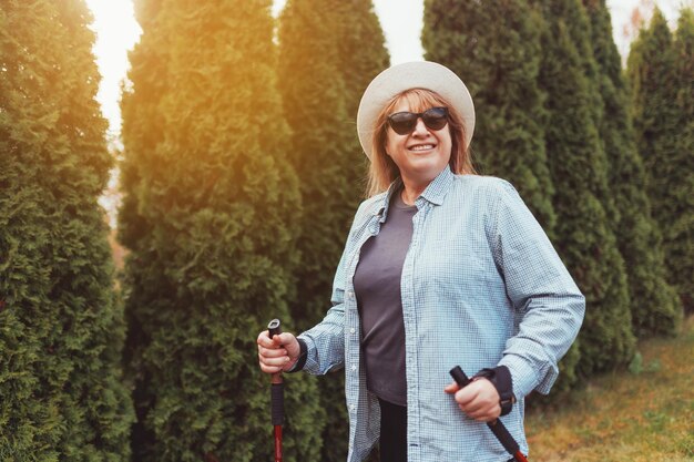 Outdoor activities people and vacations concept Attractive short haired middle aged woman in activewear hiking in forest using poles for nordic walking doing aerobic workout enjoying nature