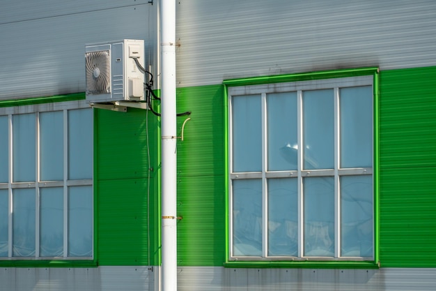 Outdoor air conditioner unit on the wall of a factory or factory The outer wall of the enterprise is made of white and green metal profiles with drain pipes and large windows space for text copy