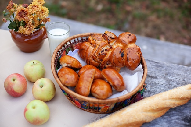 Outdoor autumn picnic with bread, a buns, applesand bouquet of flowers on wooden table