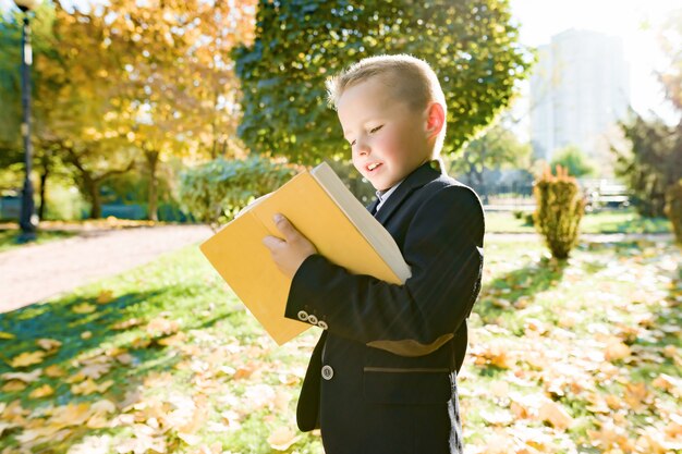 Outdoor autumn portrait of schoolboy reading book