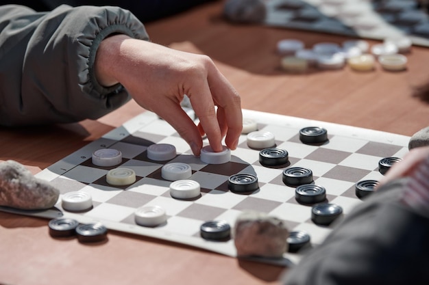 Outdoor checkers tournament on paper checkerboard on table close up players hands