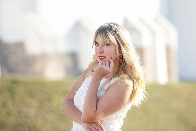 Outdoor close up portrait beautiful blonde girl with youth and skin care attractive looking at camera in white dress Light key