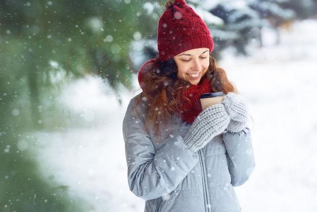 Outdoor close up portrait of young beautiful girl with hot cup of coffe. Winter holidays concept.