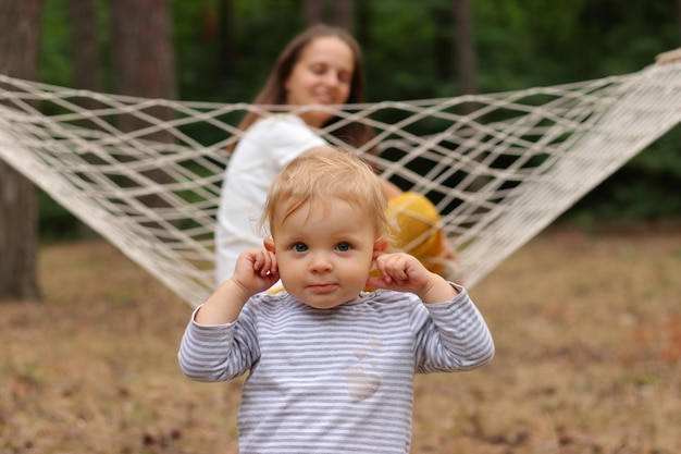 Outdoor closeup shot of cute blonde infant baby playing with mother sitting in hammock family relaxing in forest plaing in open air enjoying summer days