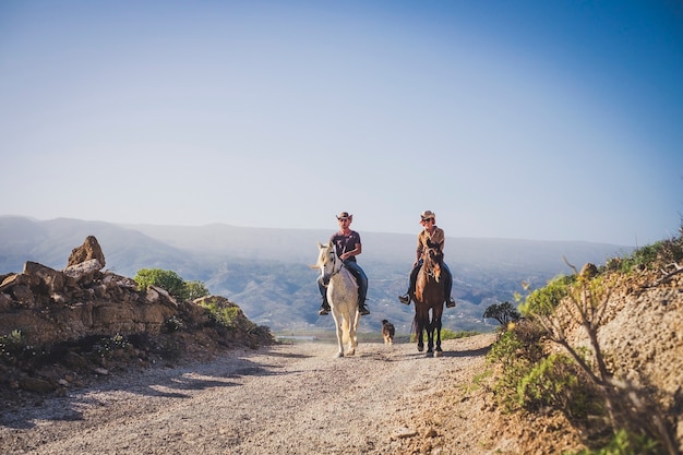 outdoor cowboy life couple ride horses at the mountain enjoying excursion in the nature together - alternative vacation travel lifestyle for alternative people