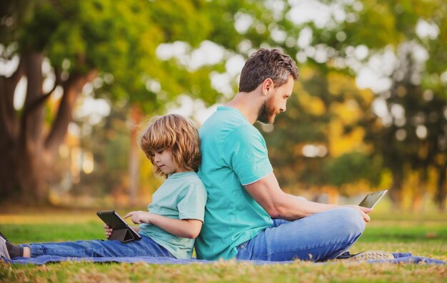 Outdoor distance learning father using laptop relax with schooler son holding laptop have fun togeth