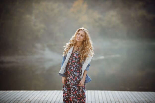 Outdoor fall portrait of girl with hat and jeans wear. Nature background, rural landscape, country style near a lake in the forest