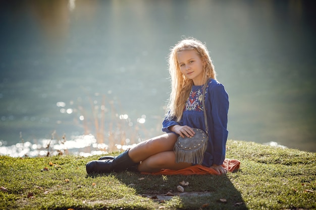 Outdoor fall portrait of girl with hat and jeans wear. Nature background, rural landscape, country style near a lake in the forest