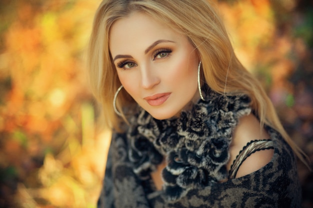 Outdoor fashion art photo of young beautiful blonde woman surrounded autumn leaves outdoor in park. Autumn season fashion 