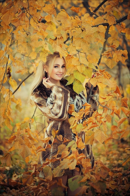 Outdoor fashion art photo of young beautiful blonde woman surrounded autumn leaves outdoor in park. Autumn season fashion 