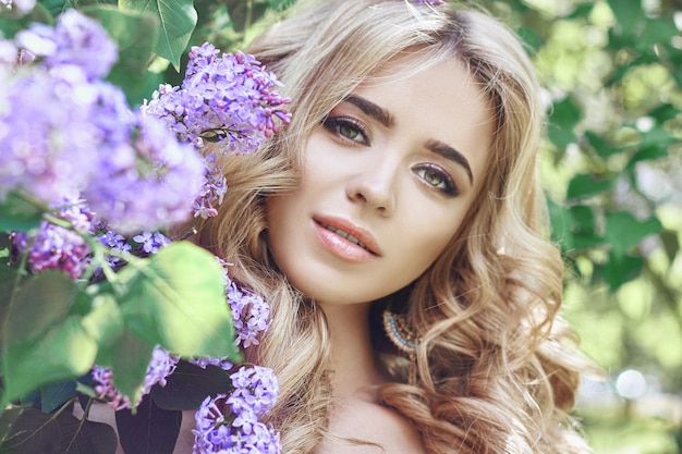 Moda all'aperto bella giovane donna circondata da fiori lilla estate. cespuglio di lillà del fiore di primavera. ritratto di una ragazza bionda