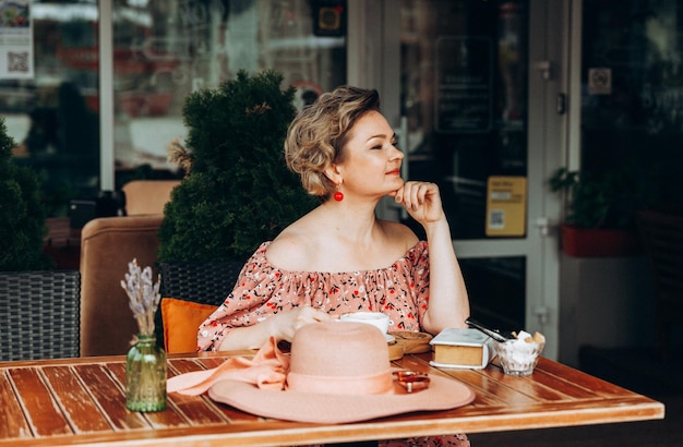 Ritratto di moda all'aperto di una splendida donna seduta in un bar bevo caffè e leggo un vecchio libro una donna con un vestito e un cappello