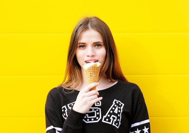 Открытый модный портрет молодой хипстерской девушки с мороженым на фоне желтой стены