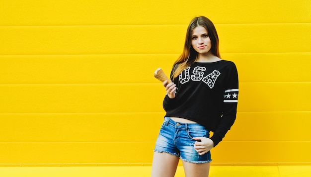 Outdoor fashion portrait of young hipster girl with  ice-cream on yellow wall background