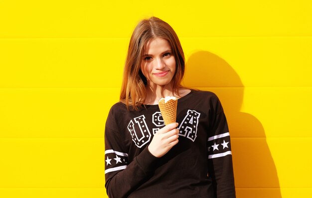 Outdoor fashion portrait of young hipster girl with ice-cream on yellow wall