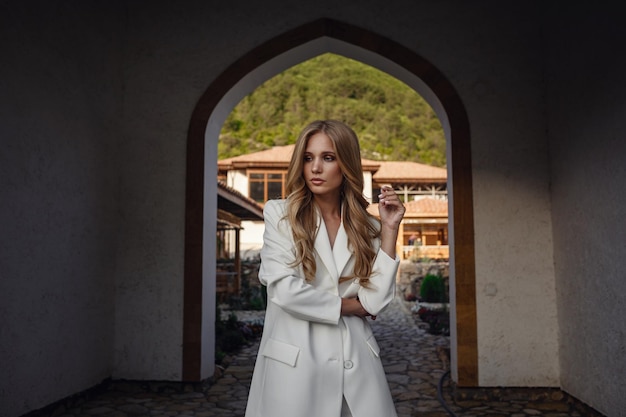 Outdoor full body fashion portrait of fashionable woman in white suit posing in street of east city Beautiful stylish shot of a tanned blonde for a fashion magazine