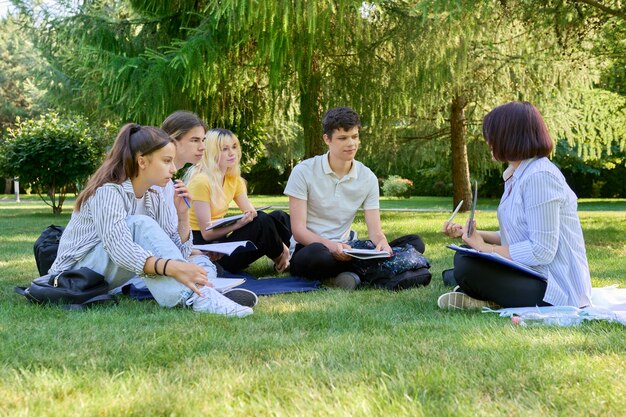 여교사가 풀밭에 앉아 있는 야외 학생들