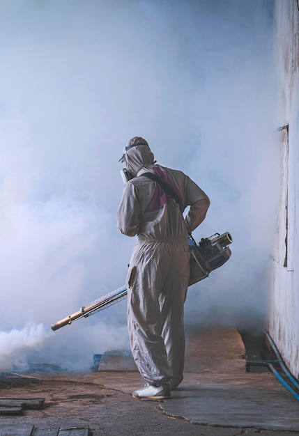 Outdoor healthcare worker using fogging machine spraying\
chemical to eliminate mosquitoes at slum