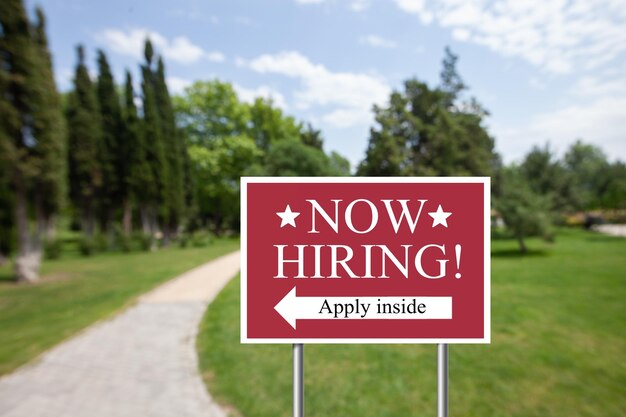 Outdoor lawn sign now hiring apply inside with a direction\
arrow. employment, understaffed business