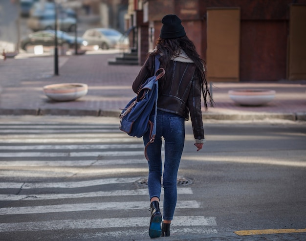 Photo outdoor lifestyle portrait of pretty young girl, wearing in hipster swag grunge style on urban background. wearing hat and jeans with backpack. spring fashion woman. toned style instagram filters.