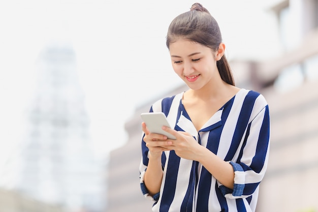 スマートフォンを探している屋外のライフスタイルの若い女性