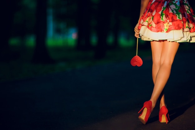 Outdoor modieuze meisje in de buurt van straat muur benen in rode schoenen met hoge hakken en korte gestreepte jurk.