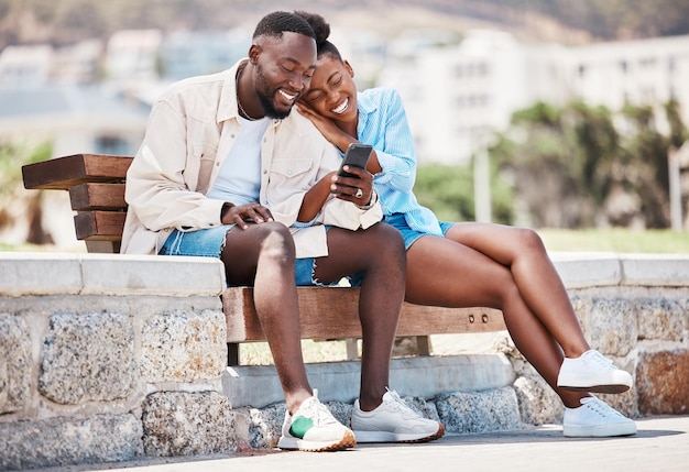 Outdoor park smartphone and couple watching online video content funny meme or social media post together on bench Happy relax and in love man and woman browsing internet on summer weekend break