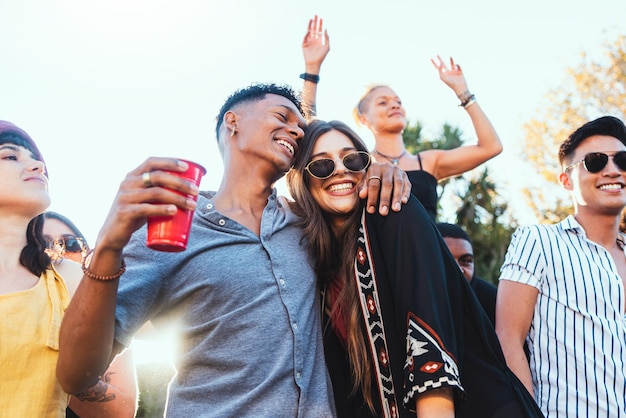 Outdoor party drinks and a couple of friends celebrate at festival concert or summer social event Diversity young men and women people together while dancing happy and drinking alcohol in crowd