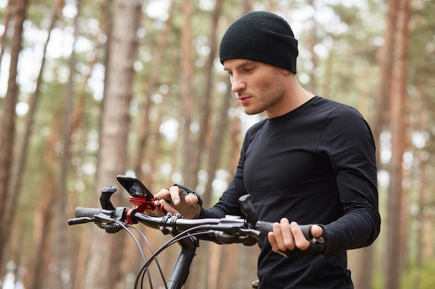 Outdoor picture of attractive young guy holding mobile phone in hands