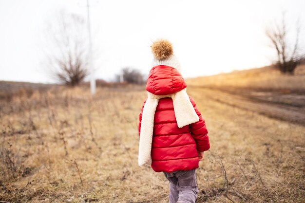 Photo outdoor picture of little girl in red coat and whit scarf from behind