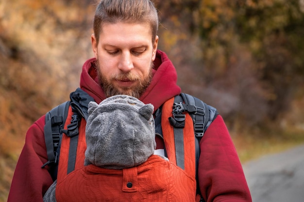 아기 슬링에 그의 아들과 함께 사랑스러운 수염된 babywearing 아버지의 야외 초상화