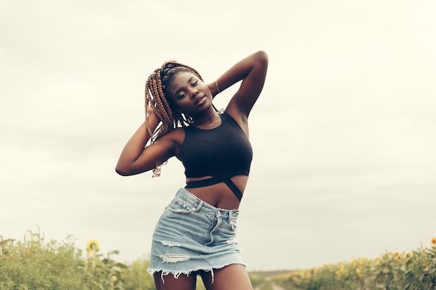 Outdoor portrait of beautiful happy mixed race African American girl teenager female young woman in a field of yellow flowers at sunset golden evening sunshine