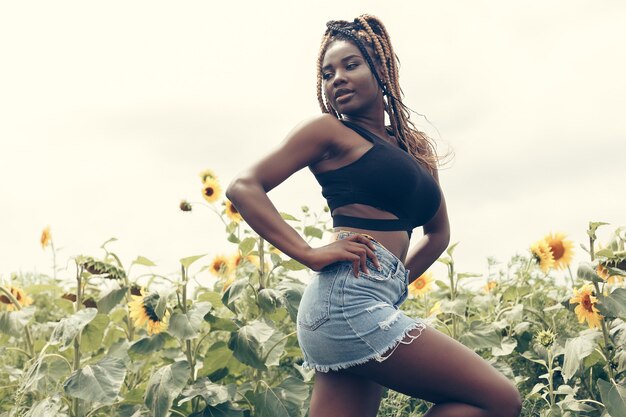 Outdoor portrait of beautiful happy mixed race African American girl teenager female young woman in a field of yellow flowers at sunset golden evening sunshine