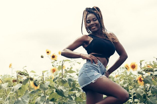 Outdoor portrait of beautiful happy mixed race African American girl teenager female young woman in a field of yellow flowers at sunset golden evening sunshine