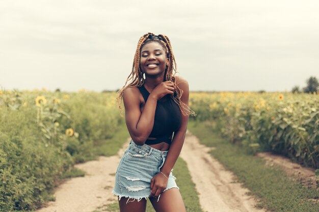 Outdoor portrait of beautiful happy mixed race African American girl teenager female young woman in a field of yellow flowers at sunset golden evening sunshine