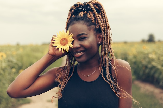 Outdoor portrait of beautiful happy mixed race African American woman in a field of yellow flowers at sunset golden evening sunshine